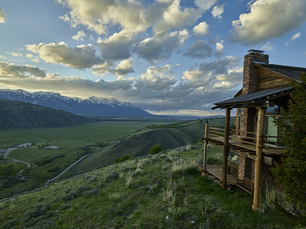 A log cabin on a bench above the valley floor in Jackson Hole, with the Teton Range across the valley
