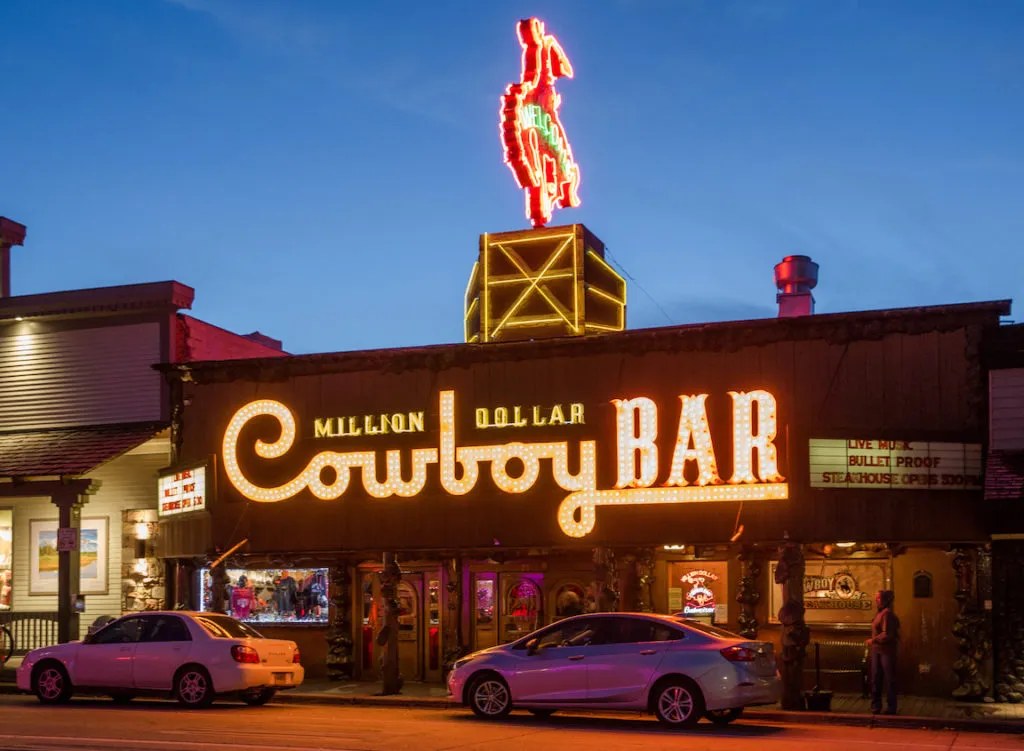 The Million Dollar Cowboy Bar on the Jackson Town Square at dusk, its neon sign lit