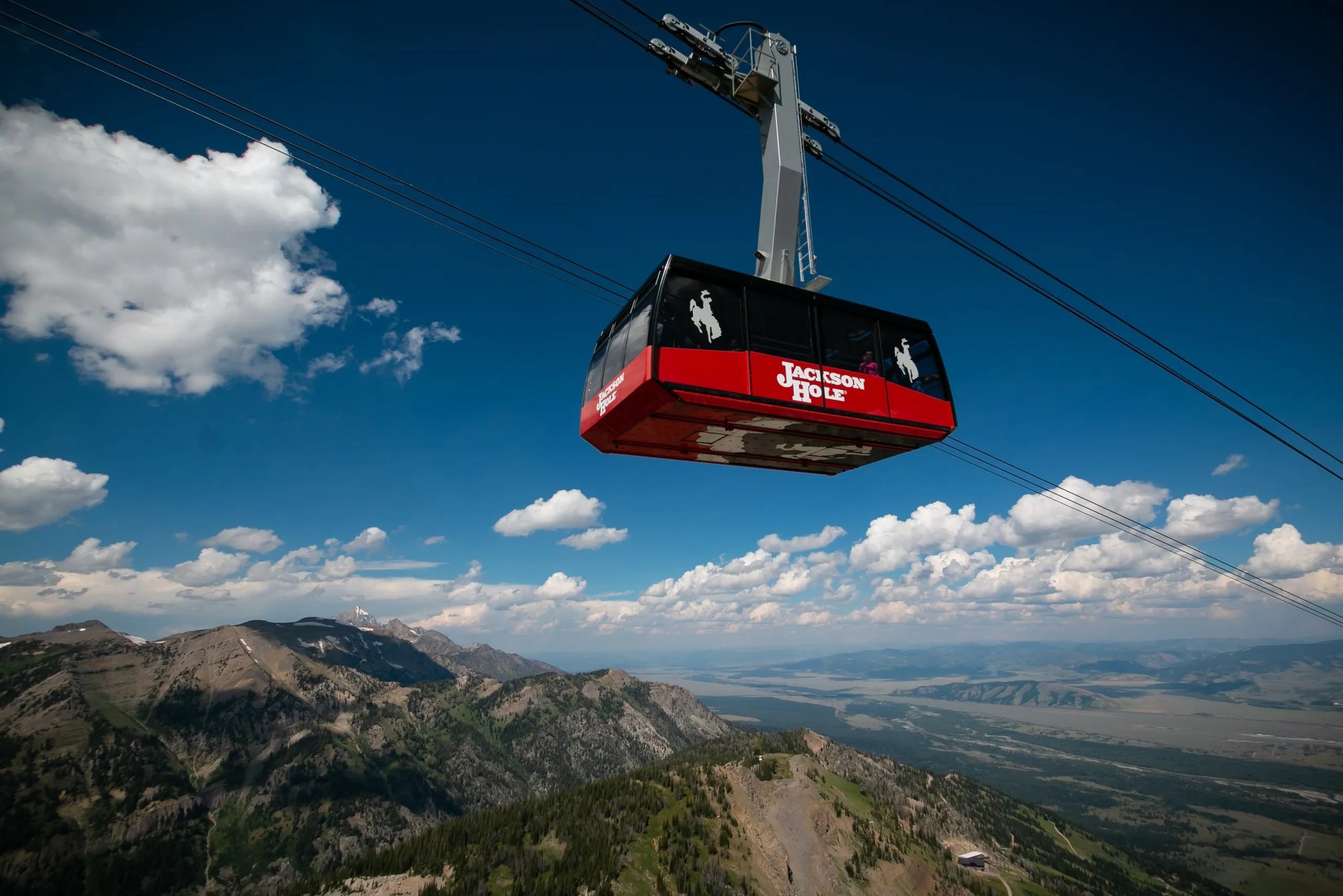 The red Jackson Hole aerial tram against a deep blue summer sky, with the Tetons and the valley floor below