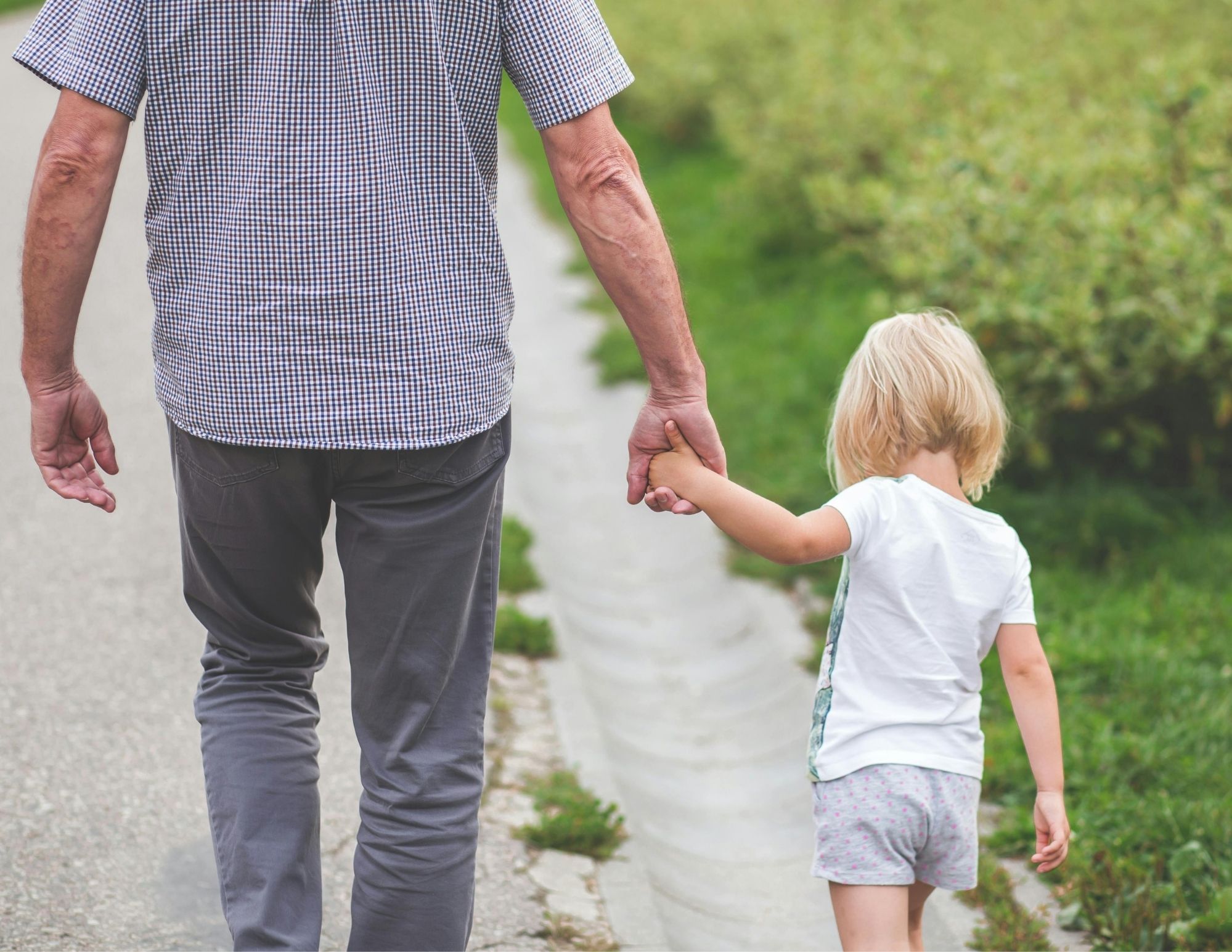 A parent in a checked shirt walking along a path holding the hand of a small child